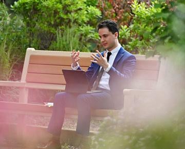 A law student participates in a Zoom call while seated outdoors. 